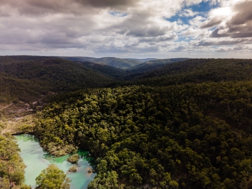 horizontal shot of a lake surrounded by bush hills with green trees on a cloudy day with grey skies - Australian Stock Image