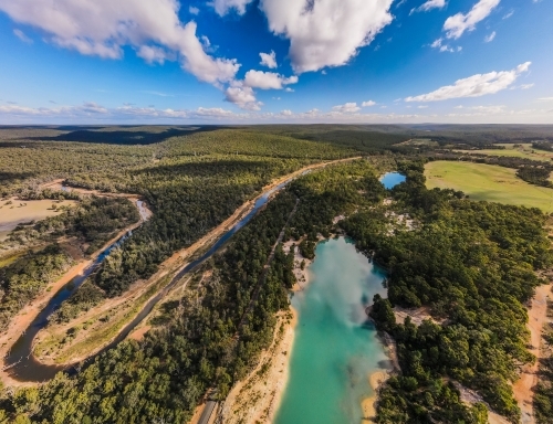 horizontal shot of a lake surrounded with green trees on a sunny day with white and blue skies - Australian Stock Image