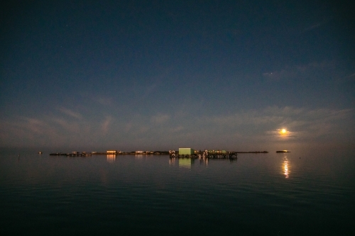 Horizontal shot of a moon setting over an island. - Australian Stock Image