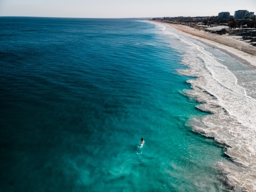 horizontal shot of a person paddling on the beach with waves on a sunny day with clear skies - Australian Stock Image