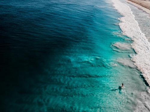 horizontal shot of a person paddling on the beach with waves on a sunny day with clear skies - Australian Stock Image