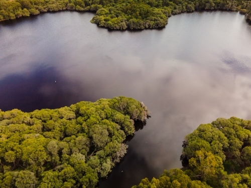 horizontal shot of a river with sky reflection between small islands with green trees and bushes - Australian Stock Image