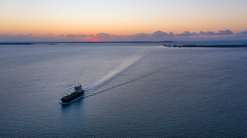 Horizontal shot of a ship sailing away from a port  at sunset - Australian Stock Image