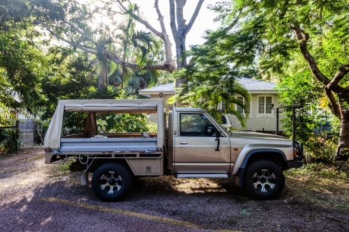 horizontal shot of a ute parked in front of house and trees in the background on a sunny day - Australian Stock Image