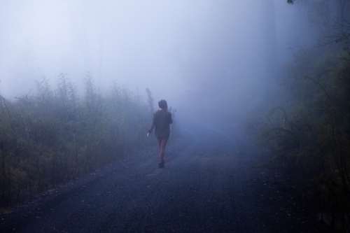 horizontal shot of a woman walking on a misty road with trees and bushes - Australian Stock Image