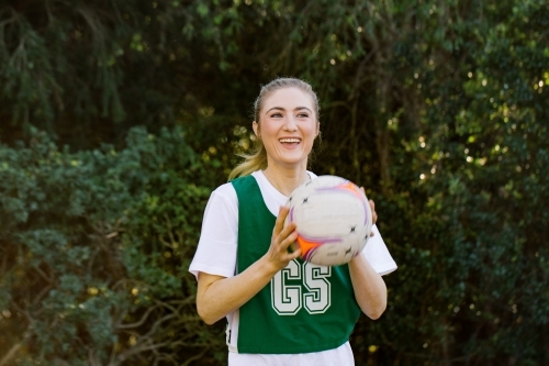 horizontal shot of a young smiling woman in sports wear holding a net ball with two hands - Australian Stock Image