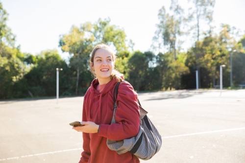 horizontal shot of a young woman smiling and looking distance wearing maroon hoodie on a sunny day - Australian Stock Image