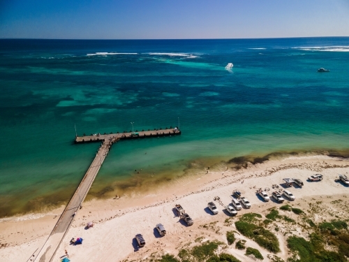 horizontal shot of cars and boats parked on a white sand with bushes, waves and wooden beach walkway - Australian Stock Image