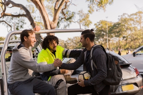 horizontal shot of men with two sitting at the back of a car while two of them shaking hands - Australian Stock Image