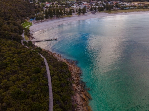 horizontal shot of ocean with sky reflection, bushes, trees, rocks, a narrow road and buildings - Australian Stock Image