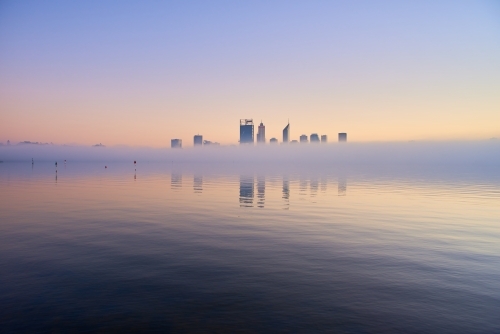 horizontal shot of Perth skyline at dawn with tiny buildings reflected on misty water - Australian Stock Image
