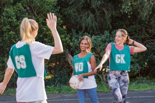 horizontal shot of three smiling young women in sports wear about to give high five to each other - Australian Stock Image