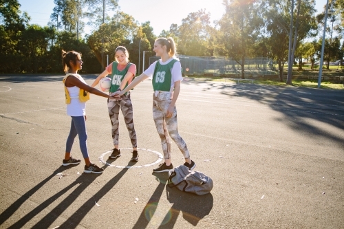 horizontal shot of three young smiling women in sports clothes stacking hands on top of each other - Australian Stock Image