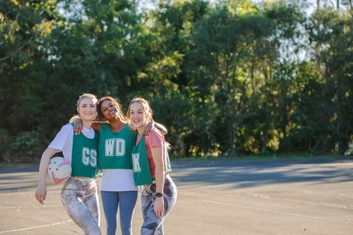 horizontal shot of three young smiling women in sports clothes with one holding a net ball - Australian Stock Image