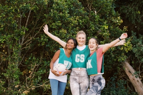 horizontal shot of three young smiling women in sports clothes with one holding a net ball - Australian Stock Image