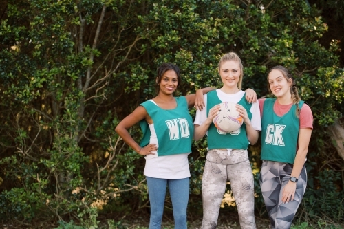 horizontal shot of three young smiling women in sports clothes with one holding a net ball - Australian Stock Image