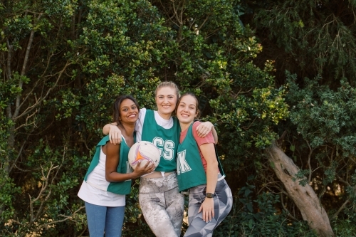 horizontal shot of three young smiling women posing for the camera with one holding a net ball - Australian Stock Image