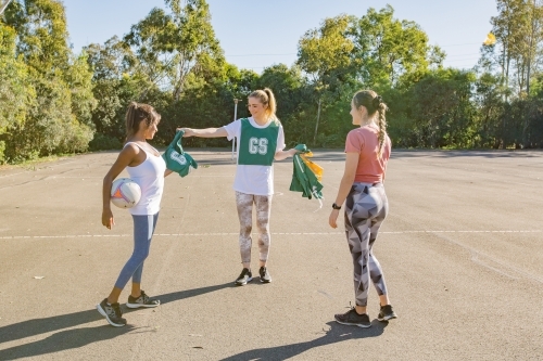 horizontal shot of three young women handing team uniforms to each other on a sunny day - Australian Stock Image