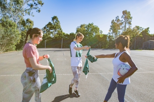 horizontal shot of three young women handing team uniforms to each other on a sunny day - Australian Stock Image