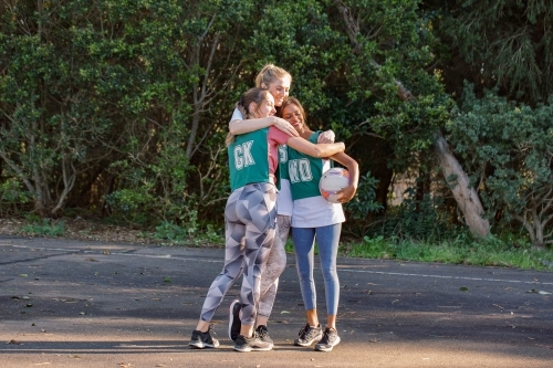 horizontal shot of three young women hugging each other while one holding a net ball on a sunny day - Australian Stock Image