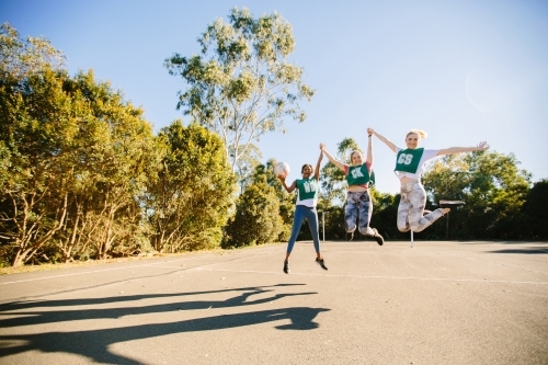 horizontal shot of three young women jumping in mid air on a sunny day with trees in the background - Australian Stock Image