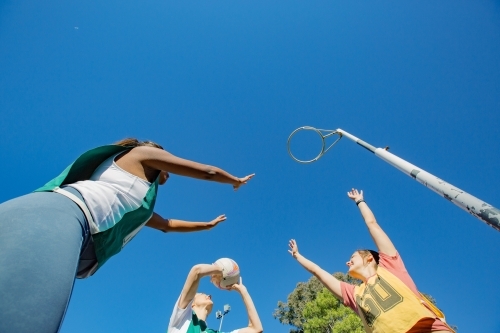 horizontal shot of three young women playing net ball on a sunny day with clear skies - Australian Stock Image