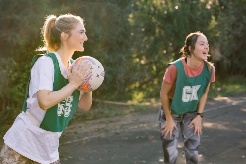 horizontal shot of two young women playing net ball in a sunny day with trees in the background - Australian Stock Image