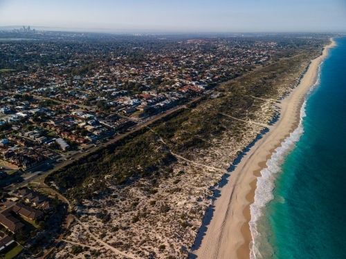 horizontal shot of white sand shoreline, green grass, ocean water, trees, roads and buildings - Australian Stock Image