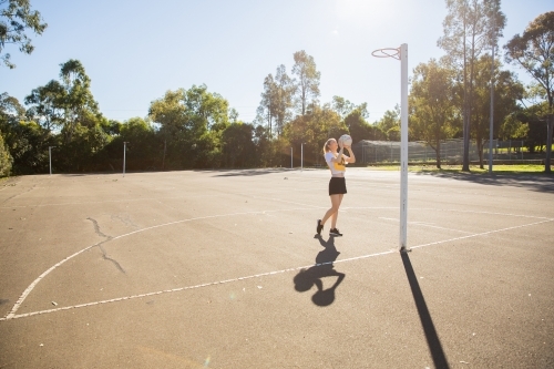 horizontal shot of young woman in sporty clothes holding a net ball in the air with one foot raised - Australian Stock Image