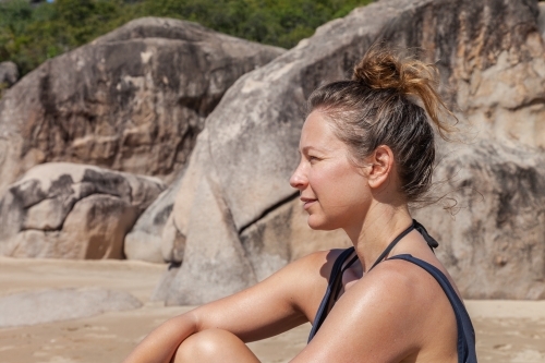 horizontal side view shot of woman sitting on a rock by the beach on a sunny day - Australian Stock Image