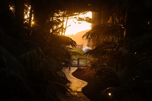 horizontal silhouette shot of a sunset with tiled walkway leaves and wooden chair outside - Australian Stock Image