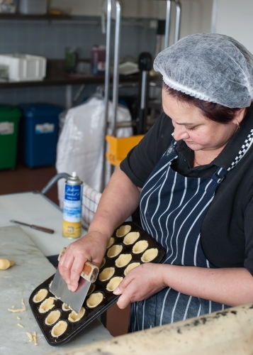 Hospitality worker cutting pastry off a baking tray - Australian Stock Image