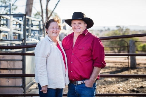 Husband and wife farmers standing on farm in drought smiling - Australian Stock Image