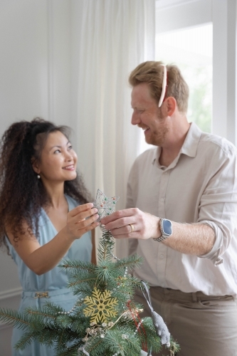 Husband and wife placing star on Christmas tree together - Australian Stock Image