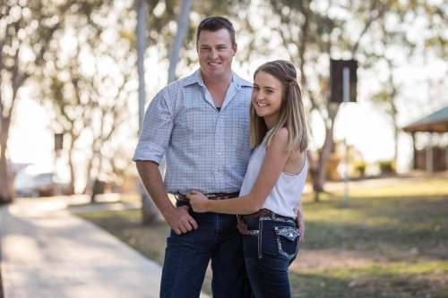 Husband and wife standing with arms around each other looking away smiling - Australian Stock Image