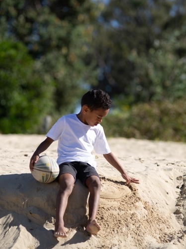 Indigenous boy playing on a sand ledge with ball - Australian Stock Image