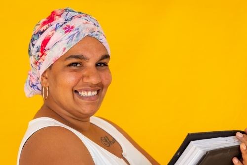 Indigenous woman wearing head wrap against a yellow background - Australian Stock Image
