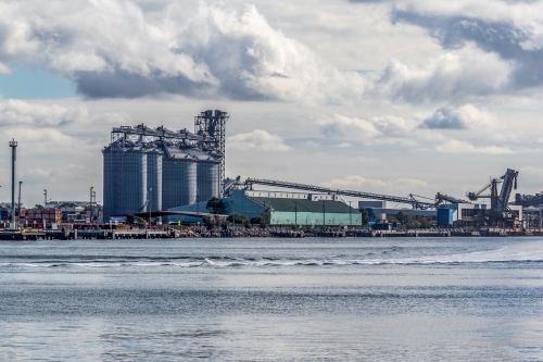 Industrial buildings and loading port along coastline in harbour - Australian Stock Image