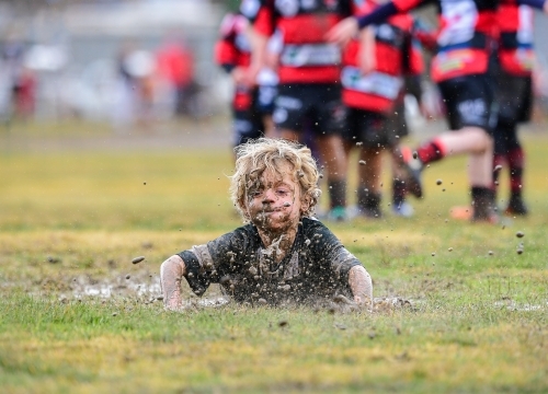 Junior rugby player belly slides in the mud - Australian Stock Image