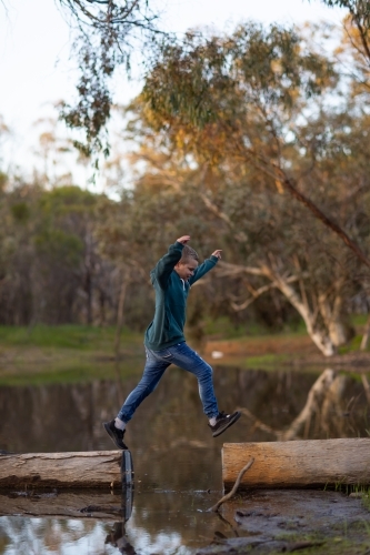 kid jumping between logs on a riverbank