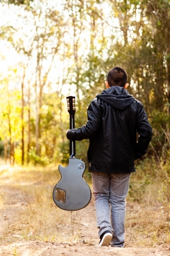 Kid with guitar walking away down path in bushland - Australian Stock Image