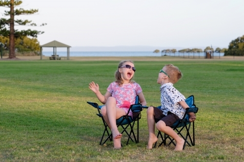 Kids having a laugh on camping chairs in the park - Australian Stock Image