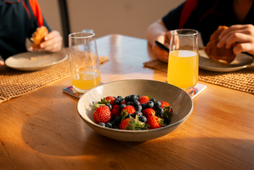 Kids in school uniform eating breakfast with fresh juice and a bowl of berries on a sunny morning. - Australian Stock Image