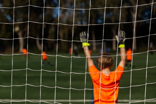 kids soccer game on a sunny day with a goalie with gloves in the air - Australian Stock Image