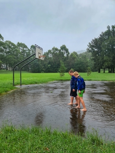 Kids walking on flooded basketball court in pouring rain - Australian Stock Image