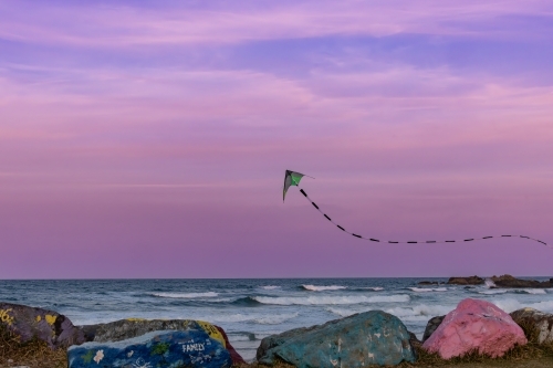 Kite flying over the Port Macquarie breakwall at sunset in pink sky - Australian Stock Image