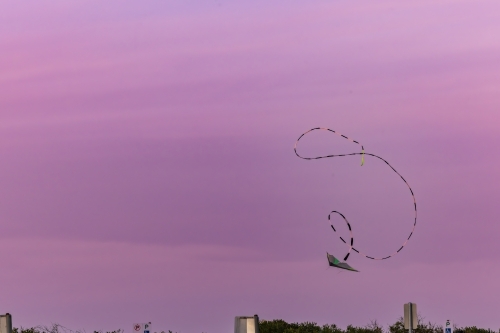 Kite flying through pink and purple sunset sky with long swirling tail - Australian Stock Image