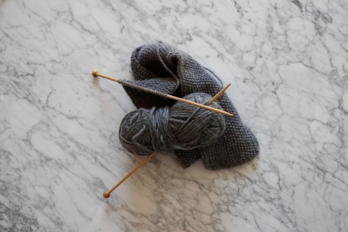 Knitting with wooden knitting needles and grey wool on marble - Australian Stock Image