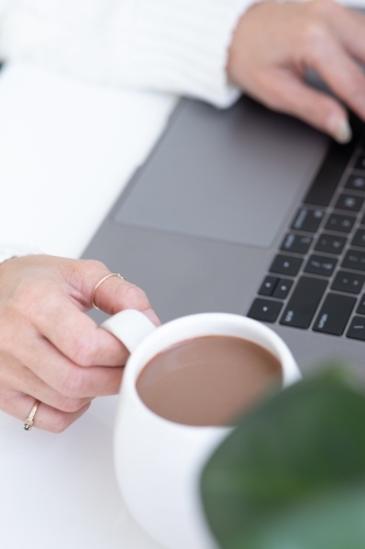 lady's hands typing on laptop with white hug mug in the foreground - Australian Stock Image