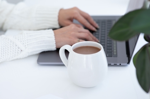 lady's hands typing on laptop with white hug mug in the foreground - Australian Stock Image